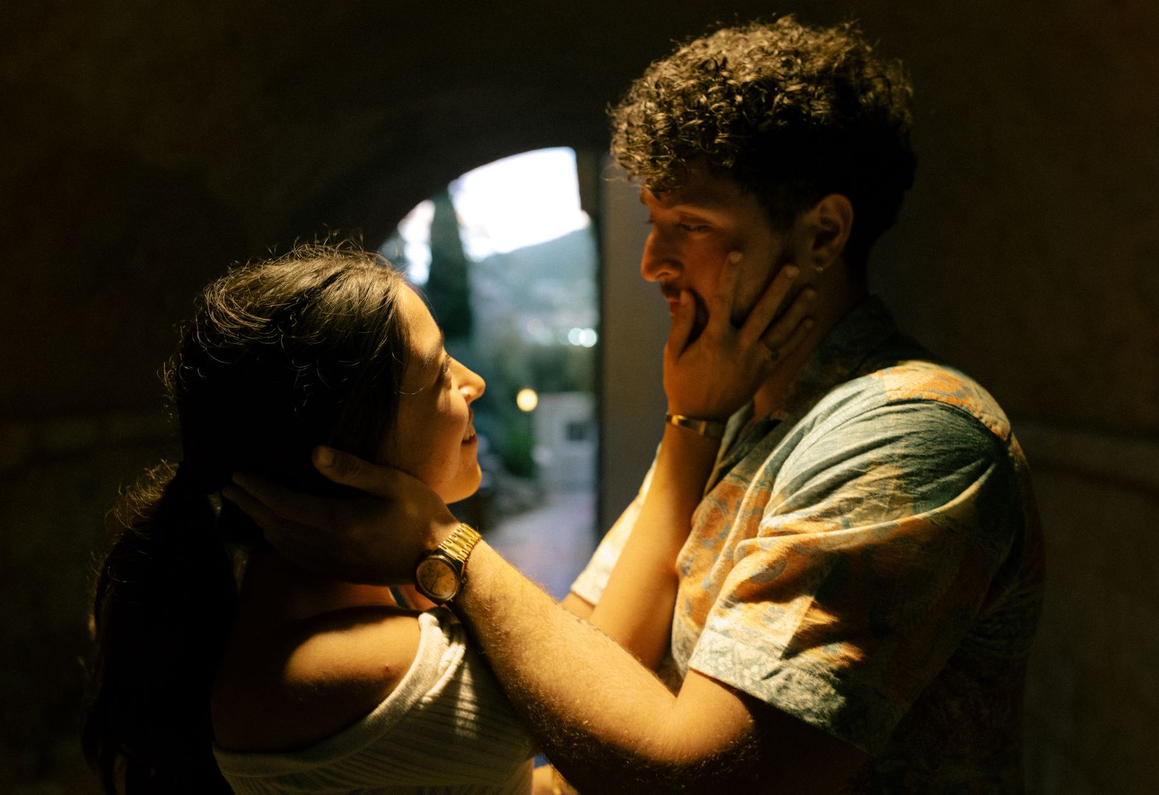 Couple dans une ruelle sombre, éclairé par une lumière blanche et se tenant mutuellement le visage dans les mains